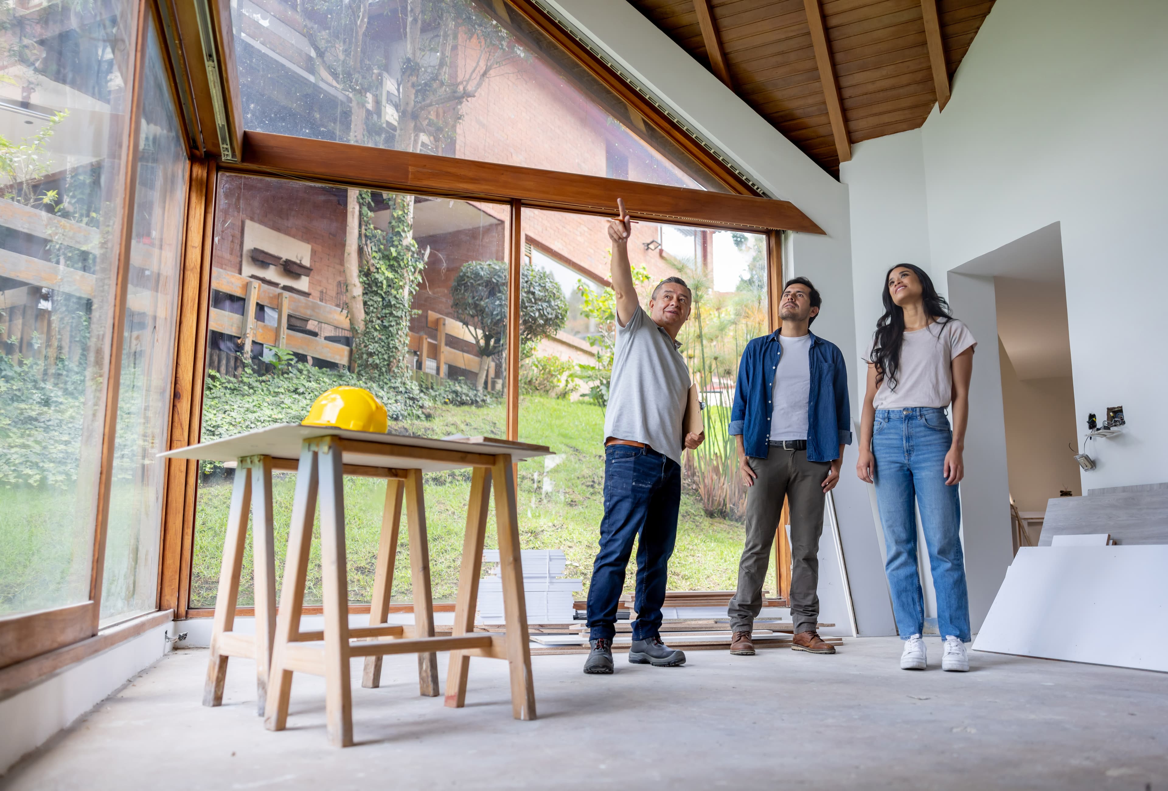 Contractor pointing out construction details to a couple inside a home with large windows